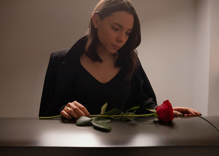 Young woman in black sitting solemnly with a red rose on a dark surface, reflecting on unhinged MILs comments.