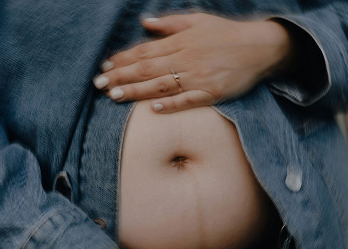 Close-up of a person’s hand with a ring resting on their bare stomach under a denim jacket, illustrating unhinged MILs comments.