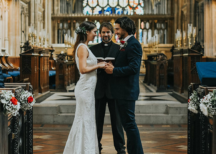 Bride and groom holding hands during a wedding ceremony with a priest in a decorated church setting about MILs unhinged comments.