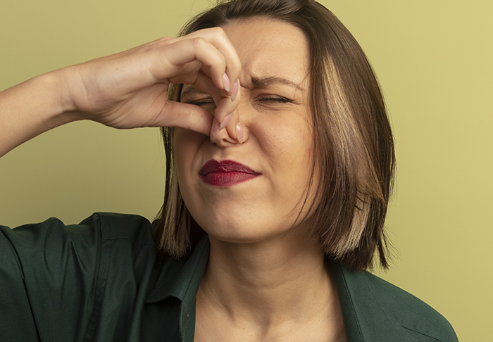 Woman pinching her nose with a disgusted expression, reacting to a mil-try-poison smell or taste.