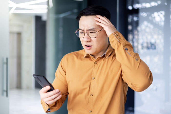 Man in glasses and mustard shirt looking shocked at phone, illustrating terrifying true stories hard to believe.