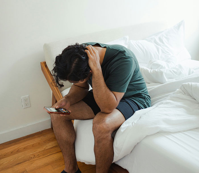 Man sitting on bed looking at smartphone, appearing stressed or thoughtful, capturing the moment of friends call two decades later. Man sitting on bed looking at smartphone, appearing stressed or thoughtful, capturing the moment of friends call two decades later.