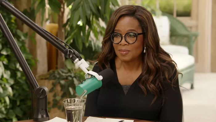 Woman with glasses speaking into a microphone, sharing stories about hidden families and mob money secrets discovered after death.