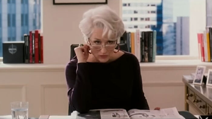Woman with white hair and glasses sitting at desk with documents, demonstrating unhinged hacks to land job strategies.
