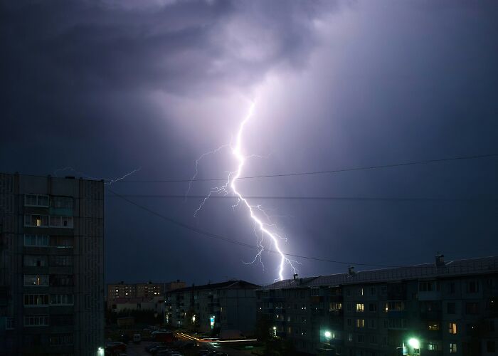 Lightning striking over residential buildings at night during a storm, illustrating true stories of people surviving crazy situations.
