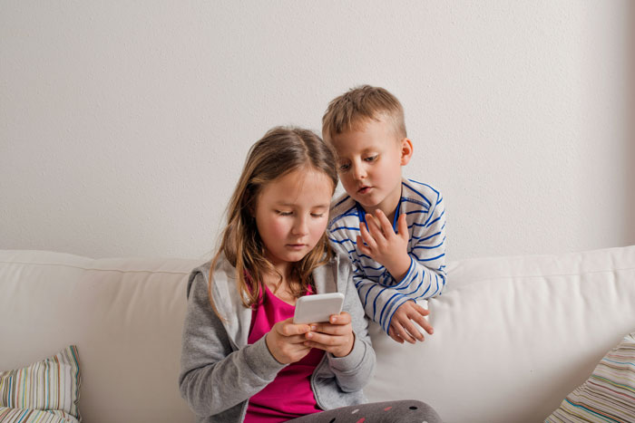 Two children sitting on a couch looking at a smartphone highlighting risks of predators targeting children's social media.