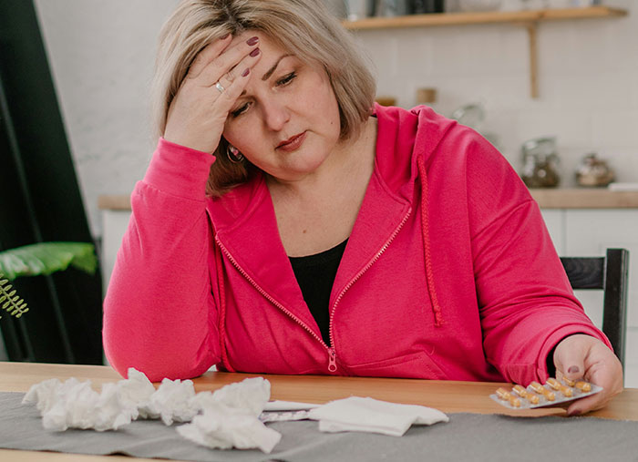 Stressed woman in pink hoodie holding medication, feeling overwhelmed after a challenging shift as a Walmart employee.