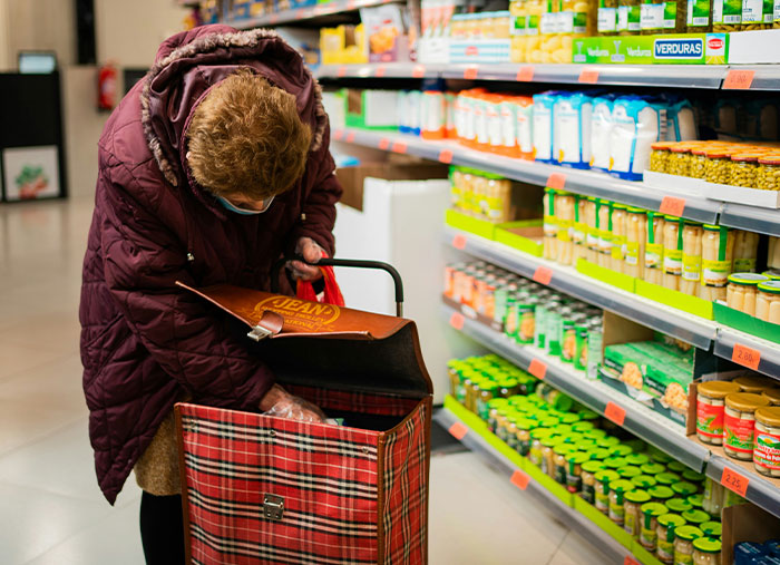 Customer shopping in grocery aisle with a plaid cart, reflecting challenges Walmart employees face at work.