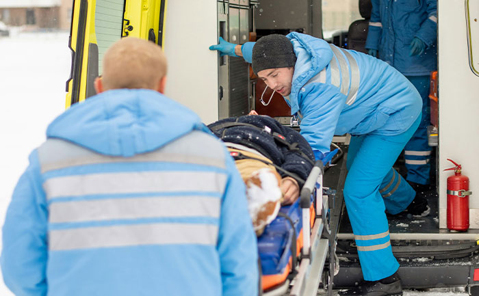 Emergency responders assisting a patient on a stretcher outside an ambulance during a snowy day at work.