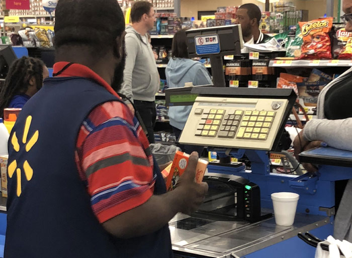 Walmart employee scanning groceries at checkout counter during a busy shift showing typical work challenges.