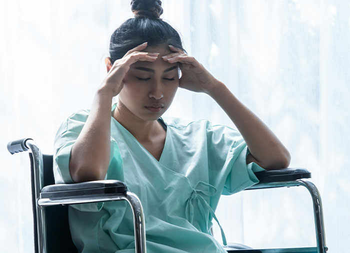 Stressed woman in hospital gown sitting in wheelchair, capturing the feeling of Walmart employees thinking I don’t get paid enough.