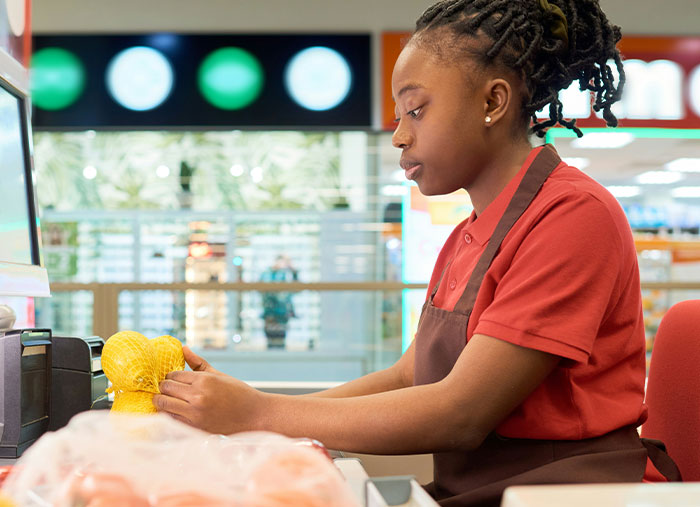 Walmart employee scanning groceries at checkout counter during a busy work shift, showing focused effort.