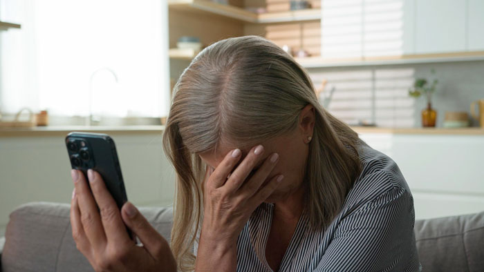 Woman stressed at home holding phone, reflecting on wearing bikini in own yard, feeling uncertain and worried.