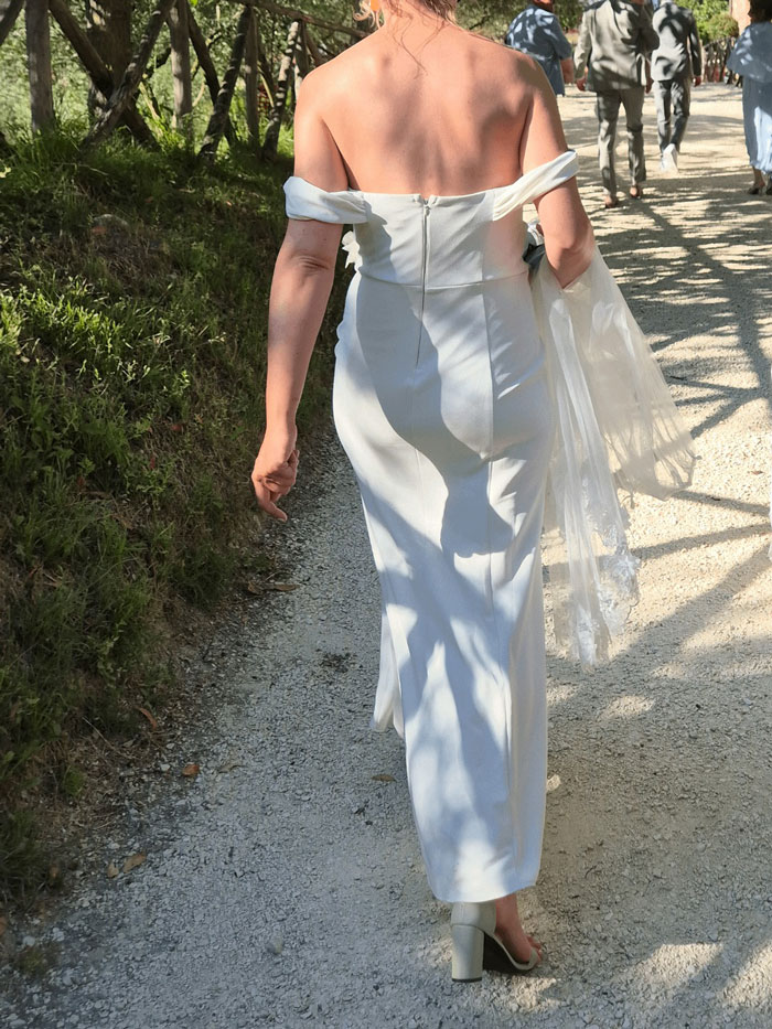 Woman in white wedding dress walking on gravel path at outdoor wedding, mistaken for sage green dress wearer.