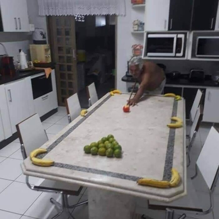Man playing pool on a kitchen table using fruit as pool balls in a daily cursed images post from IG page.
