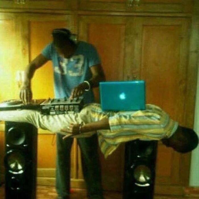 Man levitating horizontally with laptop on back while another person DJs in surreal cursed image style trending on Instagram.