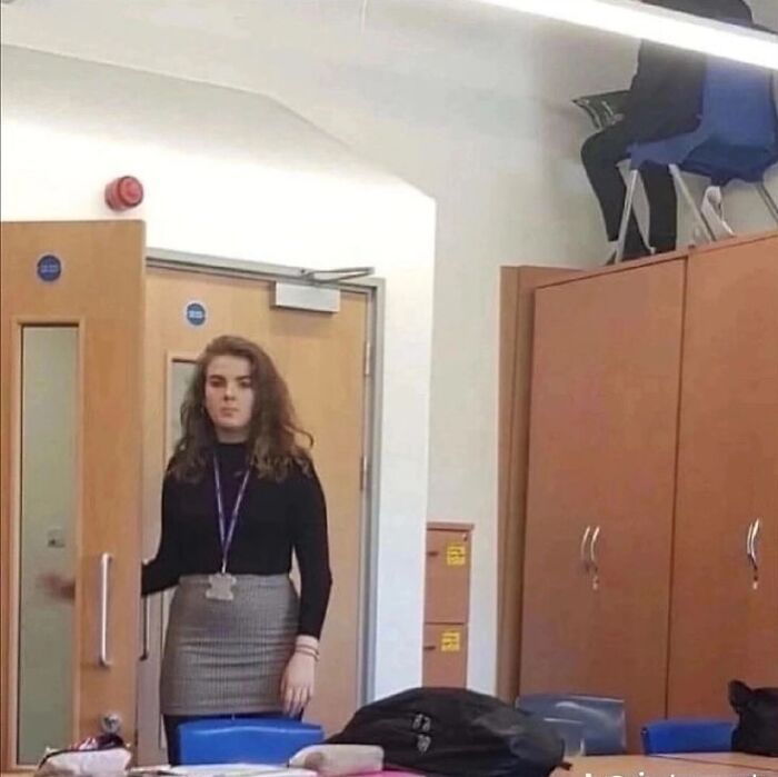 Young woman standing in a classroom with stacked chairs on top of cabinets, a cursed image from a popular IG page.