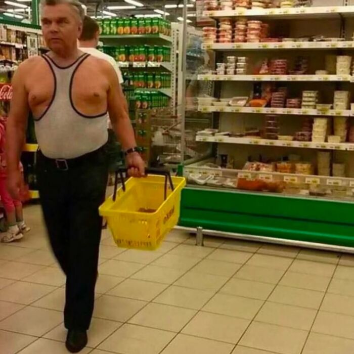Man wearing a bizarre outfit in a grocery store aisle holding a yellow shopping basket, part of cursed images collection.