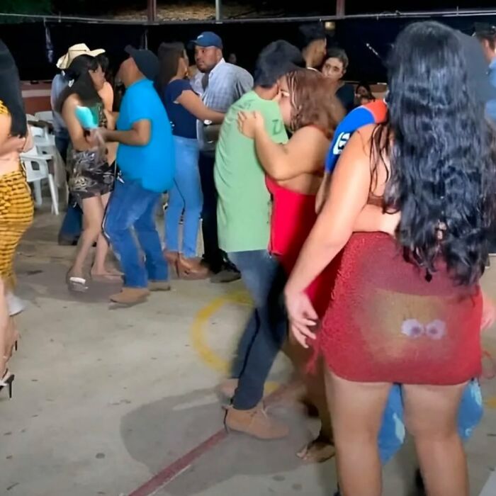 People dancing closely at a nighttime party with one woman wearing a sheer skirt showing a cursed image on her back.
