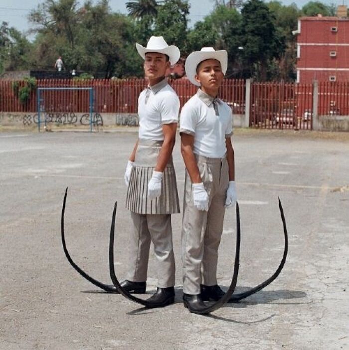 Two young men wearing white hats, gloves, and unusual costumes featuring large curved black extensions, unusual cursed image.