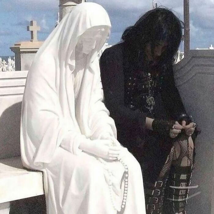 Person dressed in black sitting next to a statue holding rosary beads, a cursed image from a popular Instagram page.