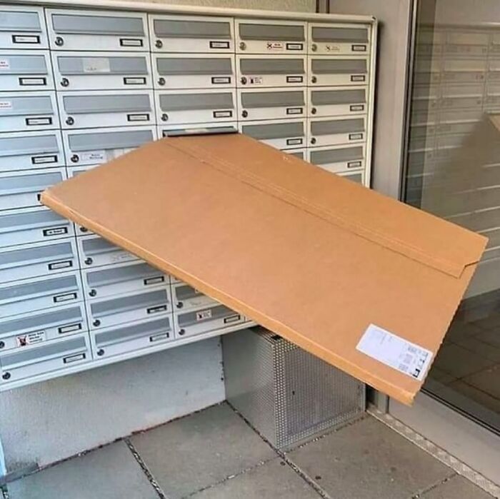 Large cardboard package awkwardly wedged across multiple mailboxes, illustrating a cursed image from a popular IG page.