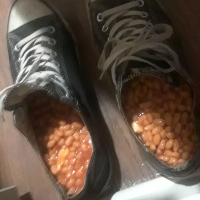 Worn black sneakers filled with baked beans on a wooden floor, an example of cursed images from a popular Instagram page.