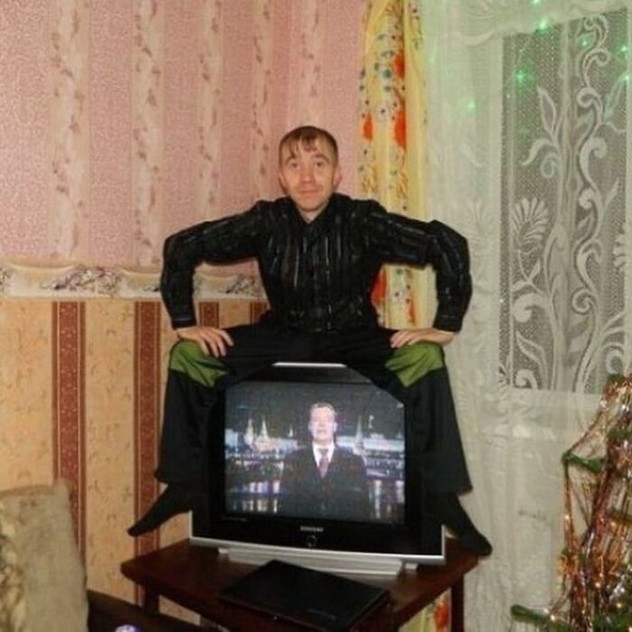 Man in black shirt sitting unusually on an old TV in a vintage room, part of cursed images disturbing fans on IG page.