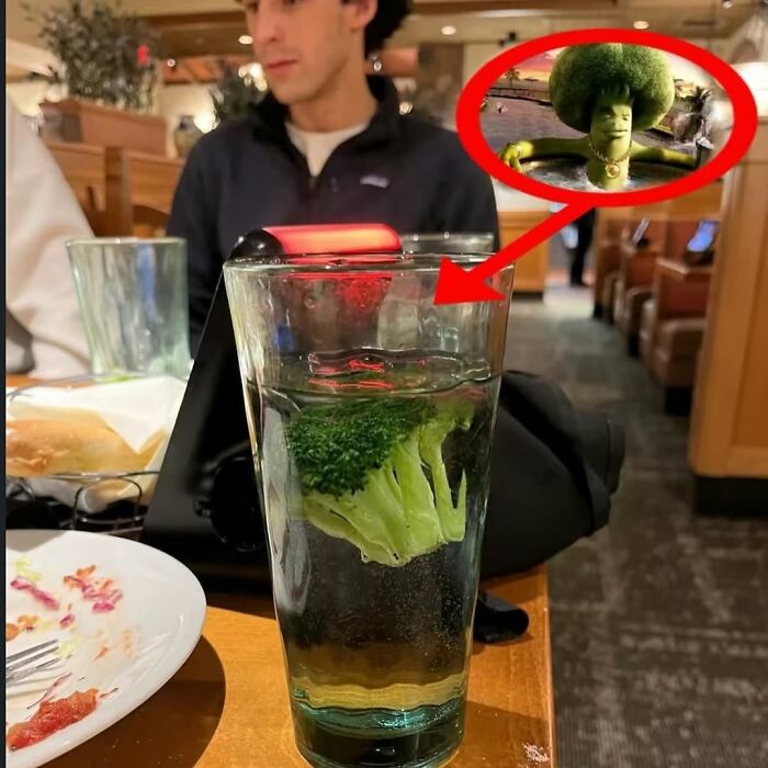 Man sitting at a table with a glass of water containing broccoli, linked to a cursed image of broccoli with a face.