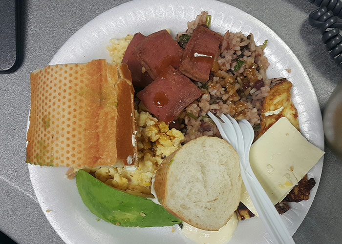 Plate of family-style breakfast with bread, scrambled eggs, fried meat, rice, and avocado, reflecting common family meals.