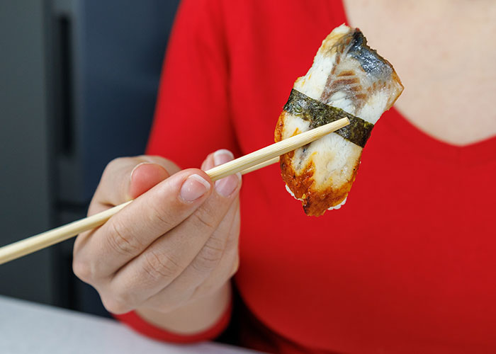 Person holding sushi with chopsticks, illustrating family traditions people assumed everyone followed.
