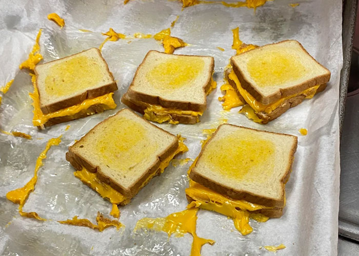 Grilled cheese sandwiches with melted cheddar on parchment paper, a common family food tradition.