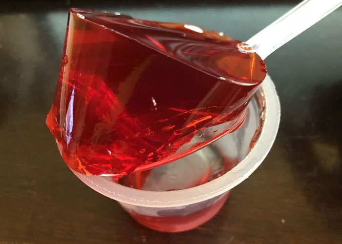 Close-up of red gelatin on a spoon above a plastic cup, representing family habits people assumed everyone did.