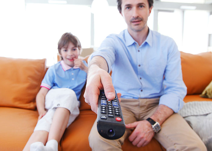 Man and child sitting on couch, using remote control, representing family habits people assumed everyone did.