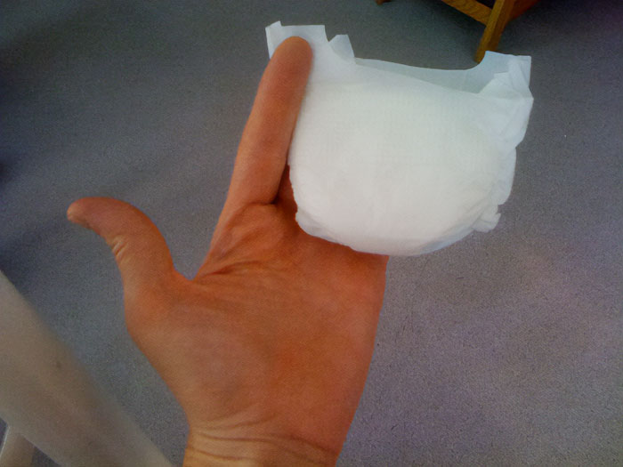 Hand holding a small folded diaper on a carpeted floor, illustrating snooping parents uncovering unexpected sides of kids.