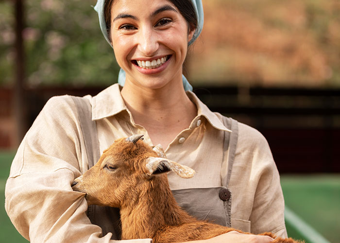 Smiling worker holding a small goat outside, illustrating people who should be paid bonuses for work madness witnessed.