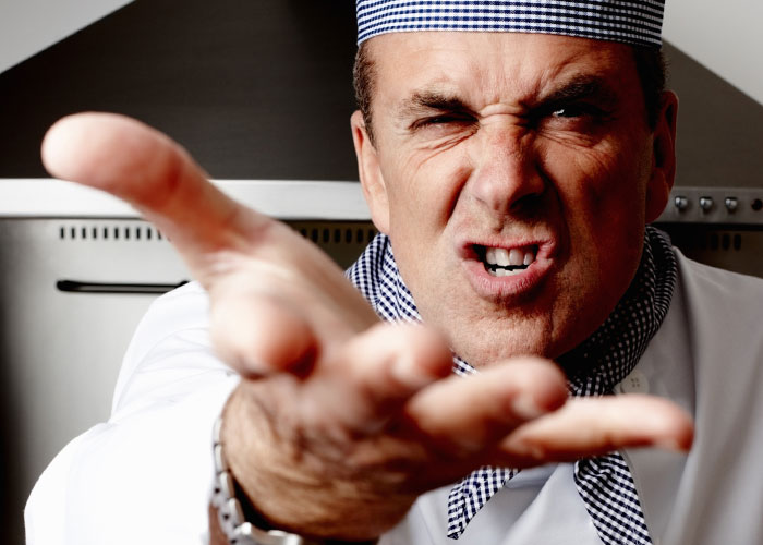 Angry chef in uniform with intense expression reaching forward, illustrating the madness people witness at work.