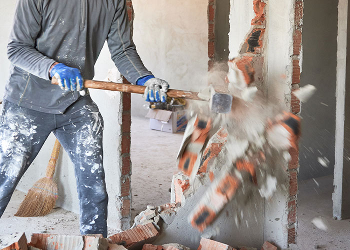 Construction worker wearing gloves demolishing a brick wall with a sledgehammer showing work site madness
