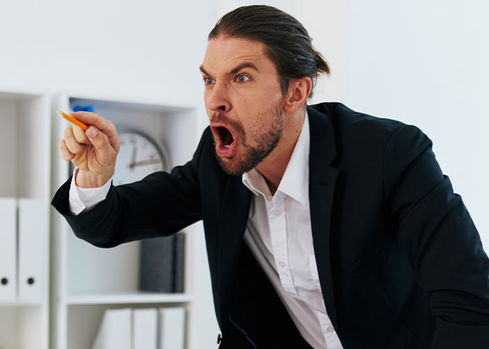 Man in a suit angrily pointing and shouting in an office, illustrating the madness some people witness at work.