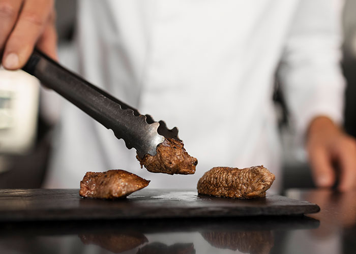 Person using tongs to handle cooked meat pieces on a dark surface, illustrating madness witnessed at work.