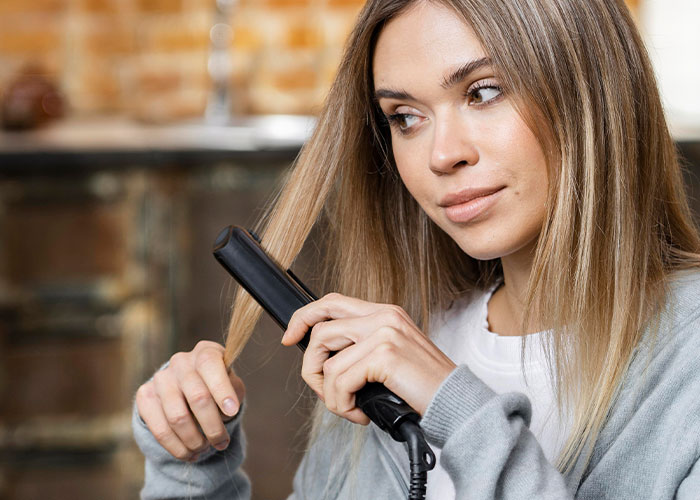 Young woman using a hair straightener at home, illustrating everyday moments related to the madness witnessed at work.