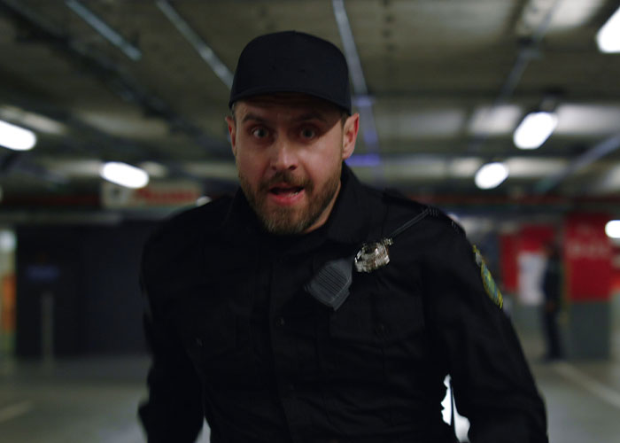 Security guard in black uniform looking alarmed in a dimly lit parking garage, witnessing absolute madness at work.