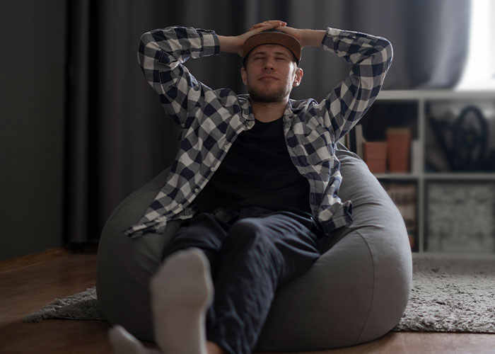 Young man relaxing on bean bag chair at home, representing people witnessing madness at work needing bonuses.
