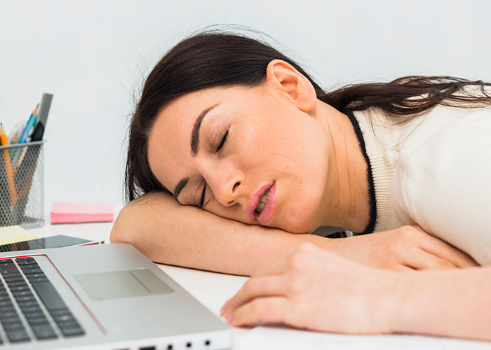 Tired woman asleep at desk next to laptop, illustrating work madness and the need for employee bonuses.