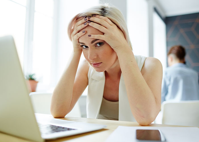 Stressed woman at work holding her head in frustration, experiencing workplace madness needing recognition and bonuses.