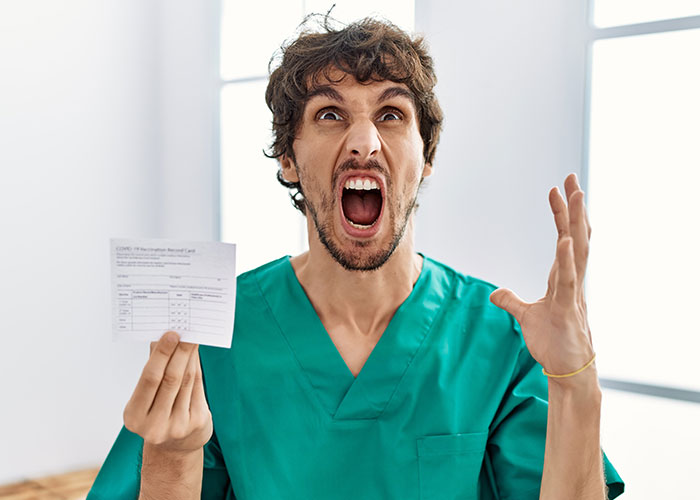 Man in green scrubs showing COVID form, expressing frustration, representing madness people witness at work.