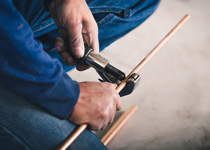 Worker using a tool to cut a copper pipe, illustrating the madness some people witness at work requiring bonuses.