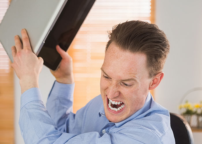 Man in blue shirt showing frustration and anger at work, capturing the madness some people face in their job environment.
