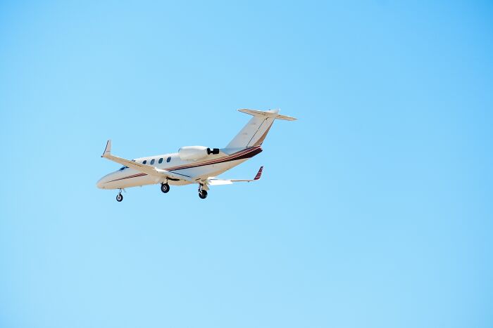 Private jet flying in clear blue sky illustrating the wealth gap and luxury lifestyle contrast.