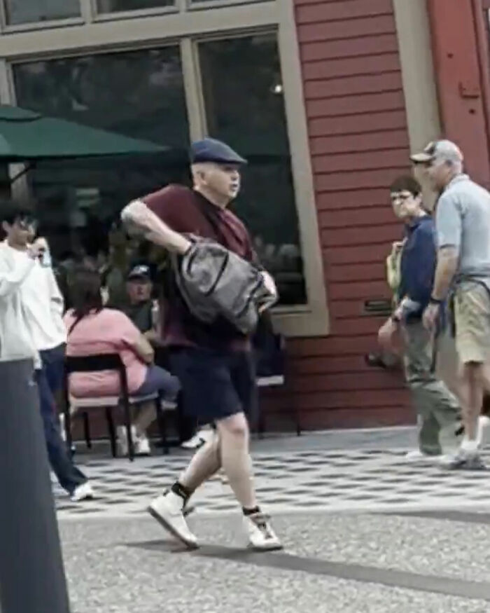 Man wearing a hat and carrying a bag walking in a public area with people around, related to shooting incident keywords. Man wearing a hat and carrying a bag walking in a public area with people around, related to shooting incident keywords.